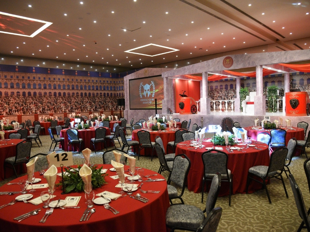 Best Events Production Partner - EVH Events. An elaborate Roman-themed corporate year-end function setup featuring a colosseum backdrop, custom stage design, and banquet tables with red settings.